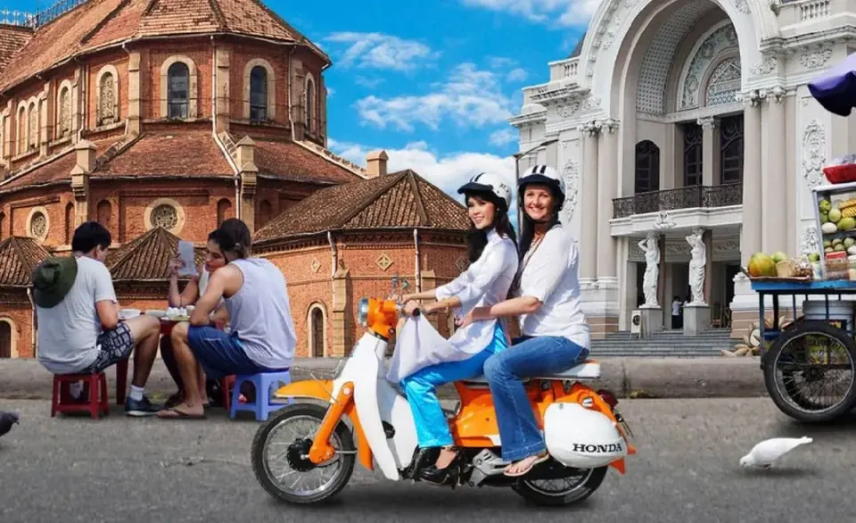Two riders on an orange Honda scooter in front of the Saigon Opera House
